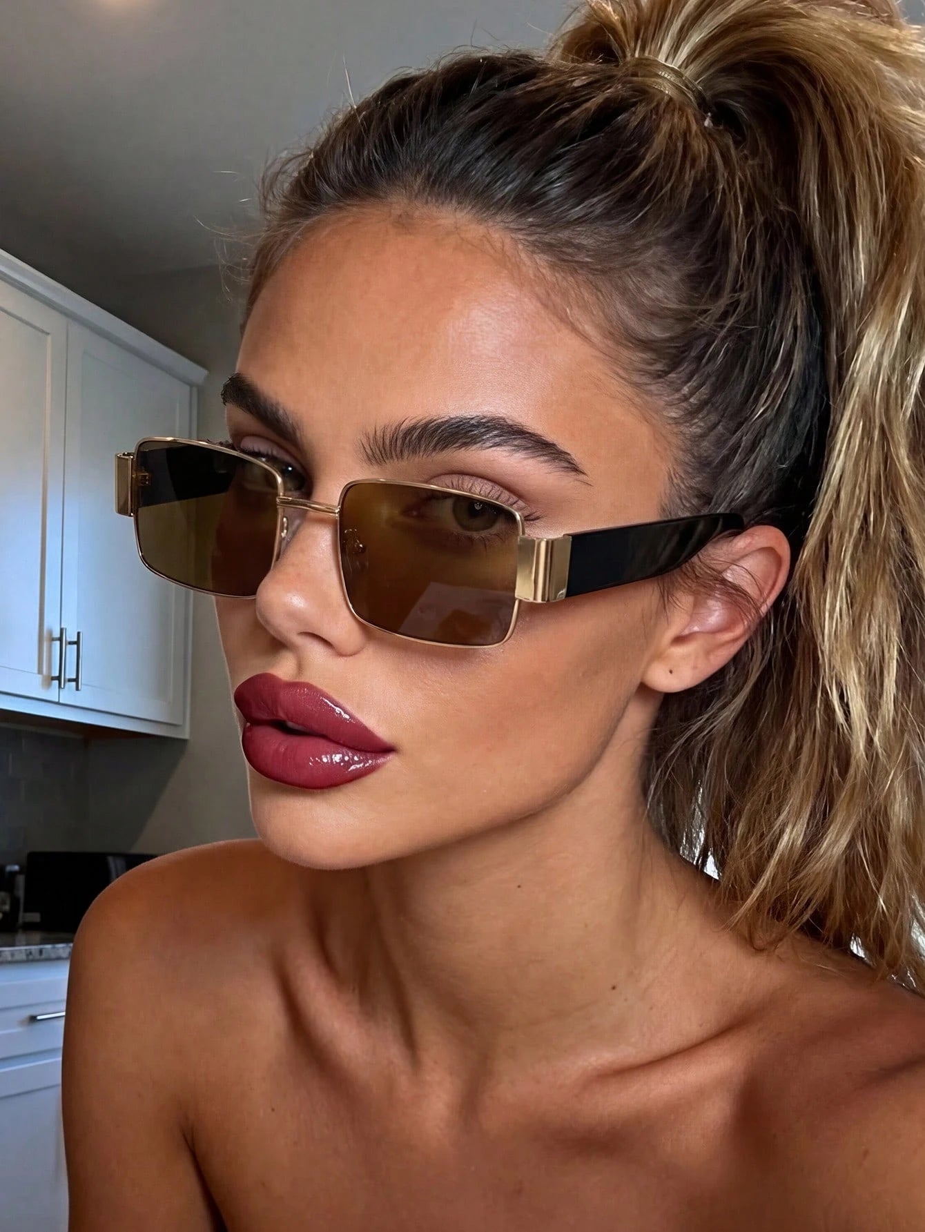 Woman wearing gold-framed sunglasses in a kitchen setting