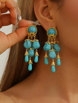 Turquoise earrings with gold accents being worn on an ear