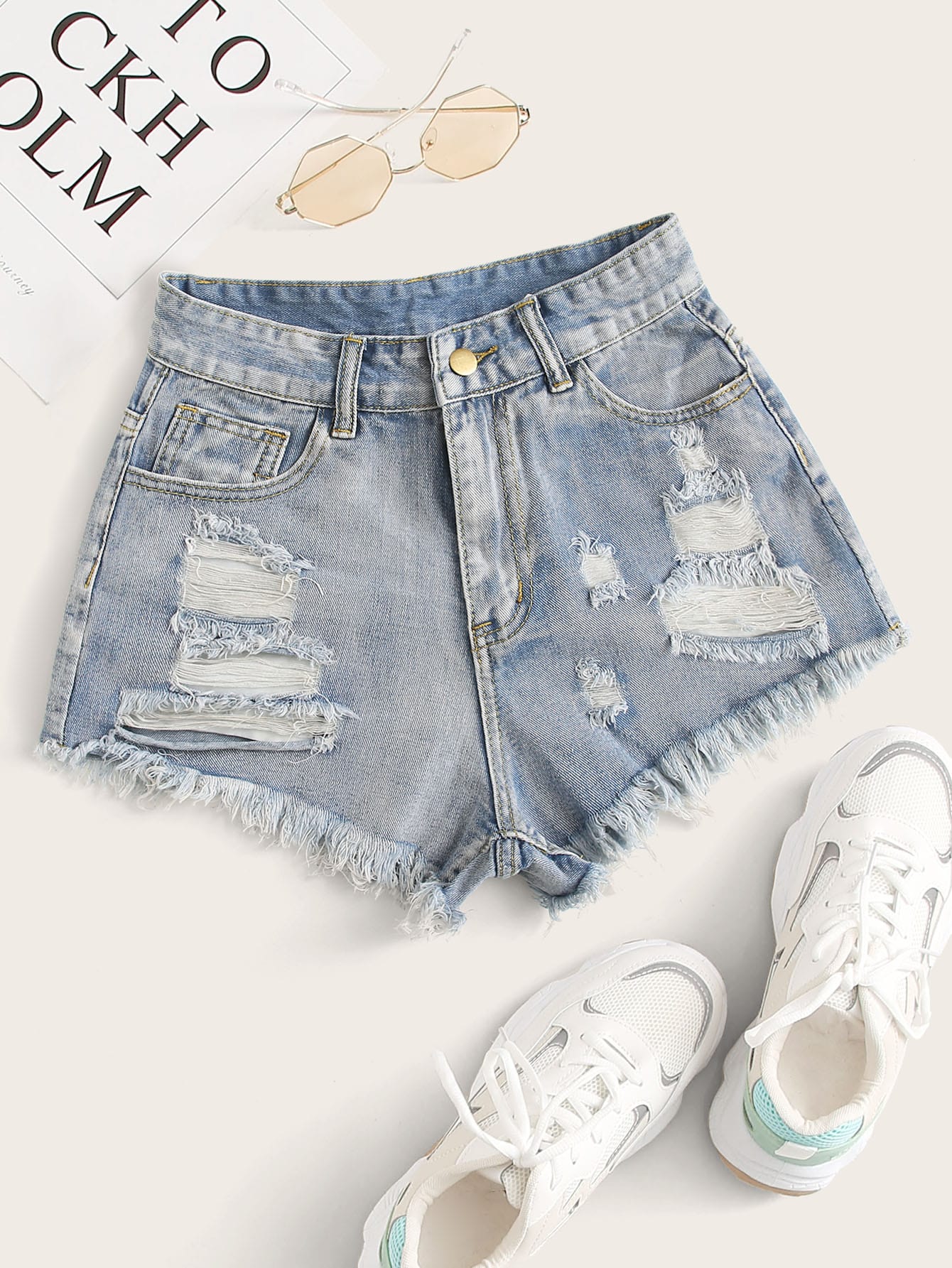 Distressed denim shorts with white sneakers on a light background