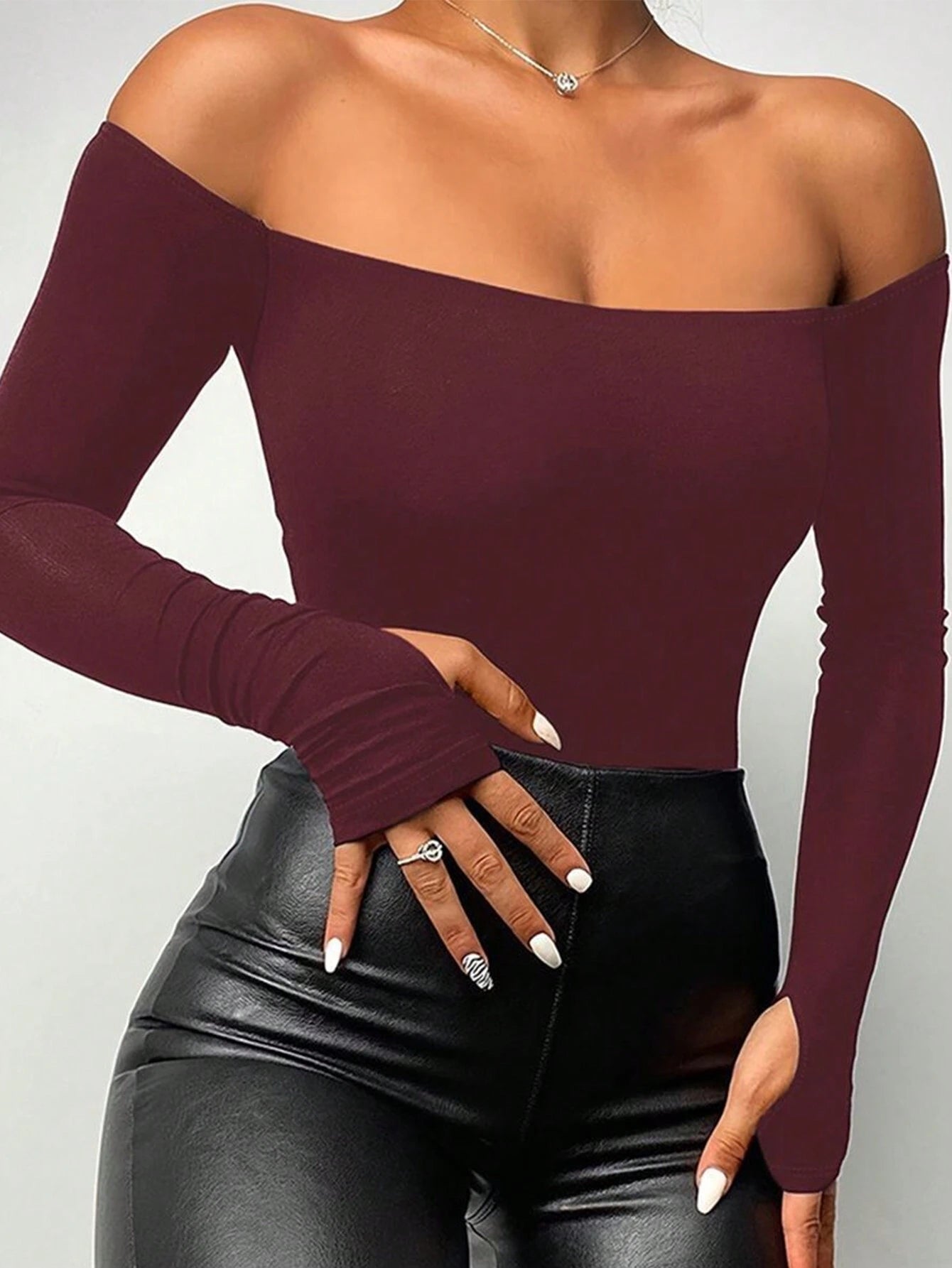 Person wearing a burgundy off-shoulder top and black leather pants on a plain background