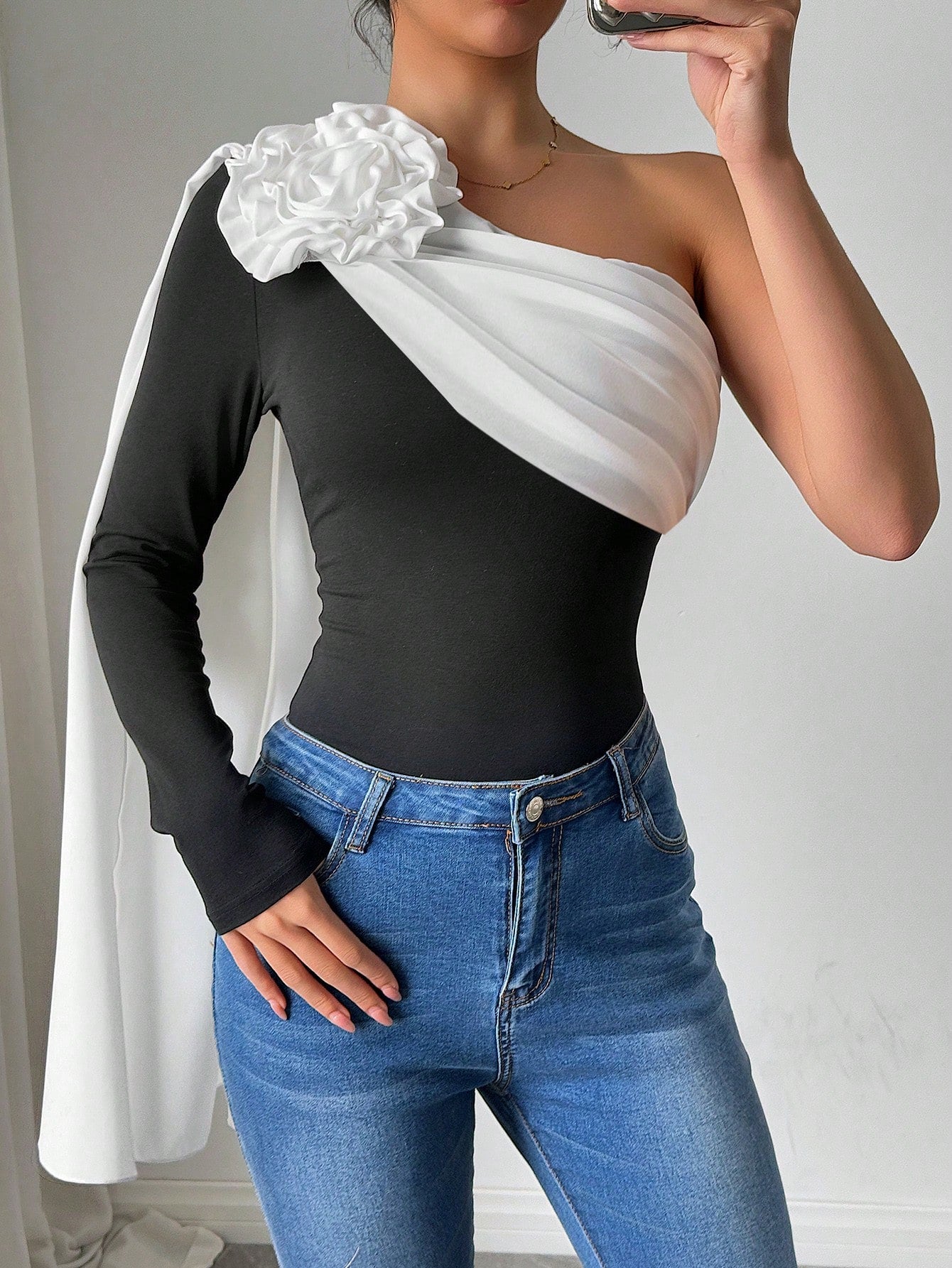 Person wearing a black and white one-shoulder top with blue jeans against a plain background