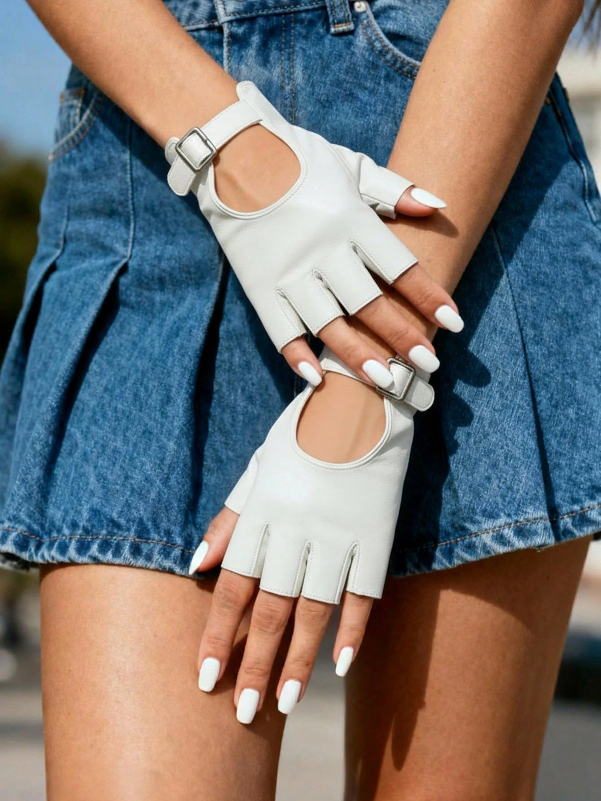 A person wearing off-white fingerless gloves with cutout details and adjustable straps, paired with a blue denim skirt.