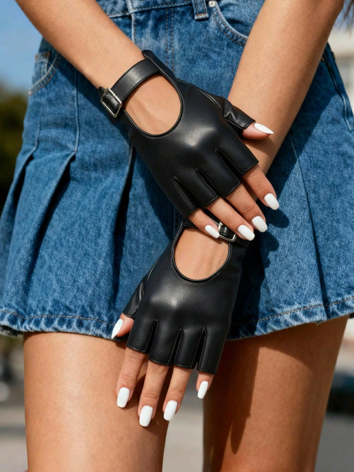 Black faux leather fingerless gloves with cutout details and adjustable buckle straps, worn by a model in a blue denim skirt.