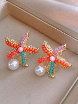 Starfish-shaped earrings with colorful beads and pearls on a beige surface