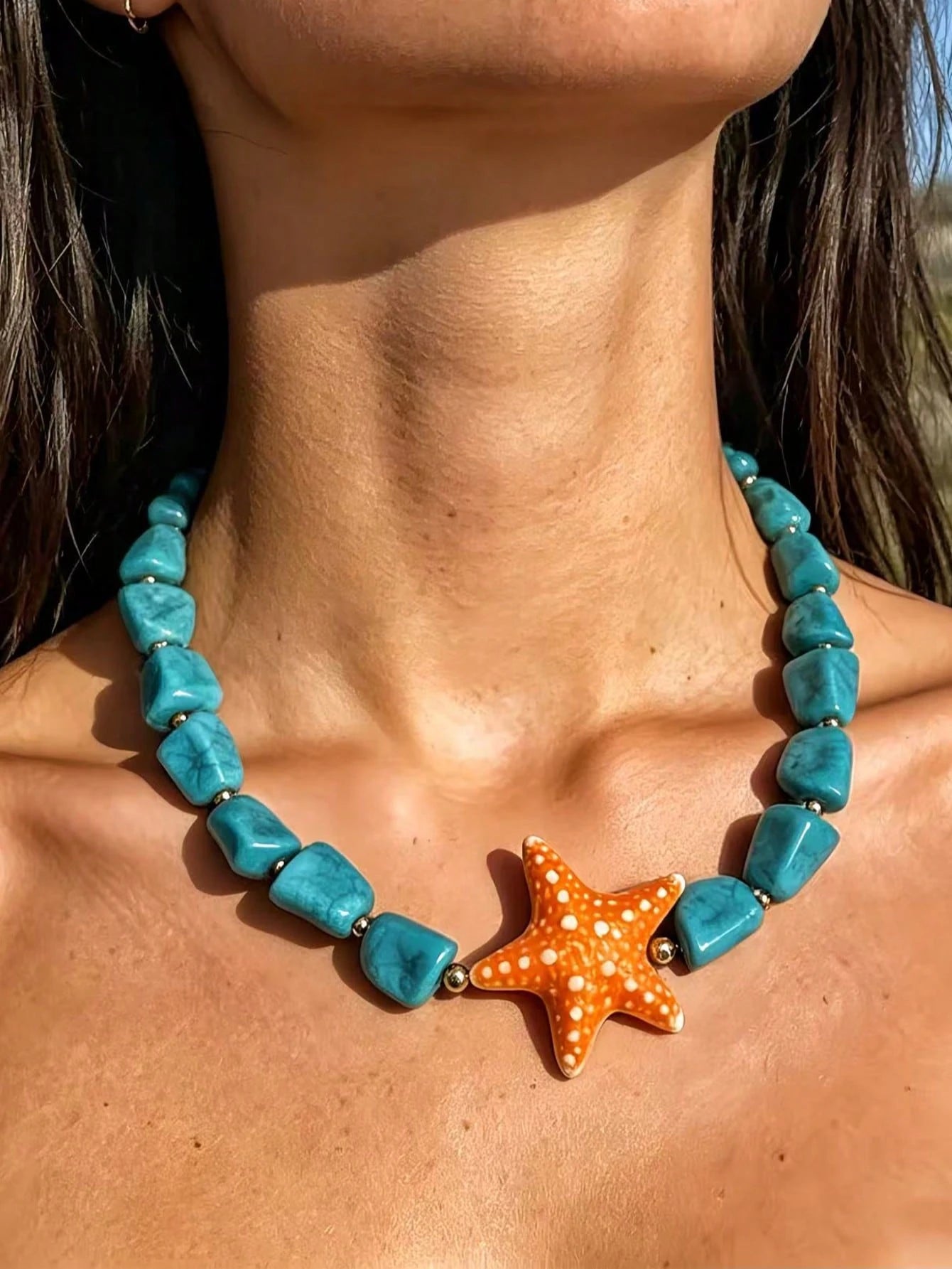 Turquoise beaded necklace with a starfish pendant worn by a person outdoors.