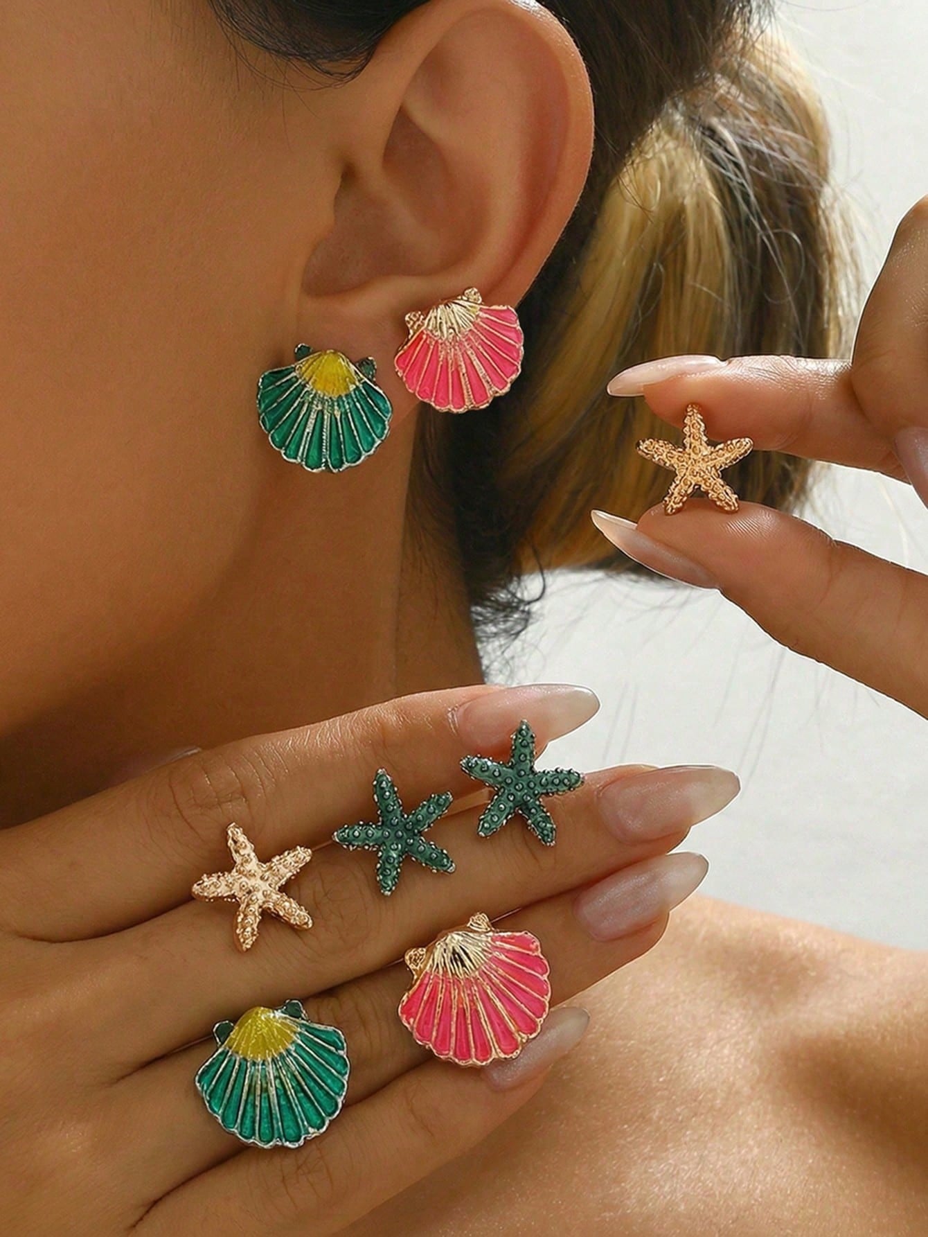 Colorful shell and starfish earrings being held near an ear.