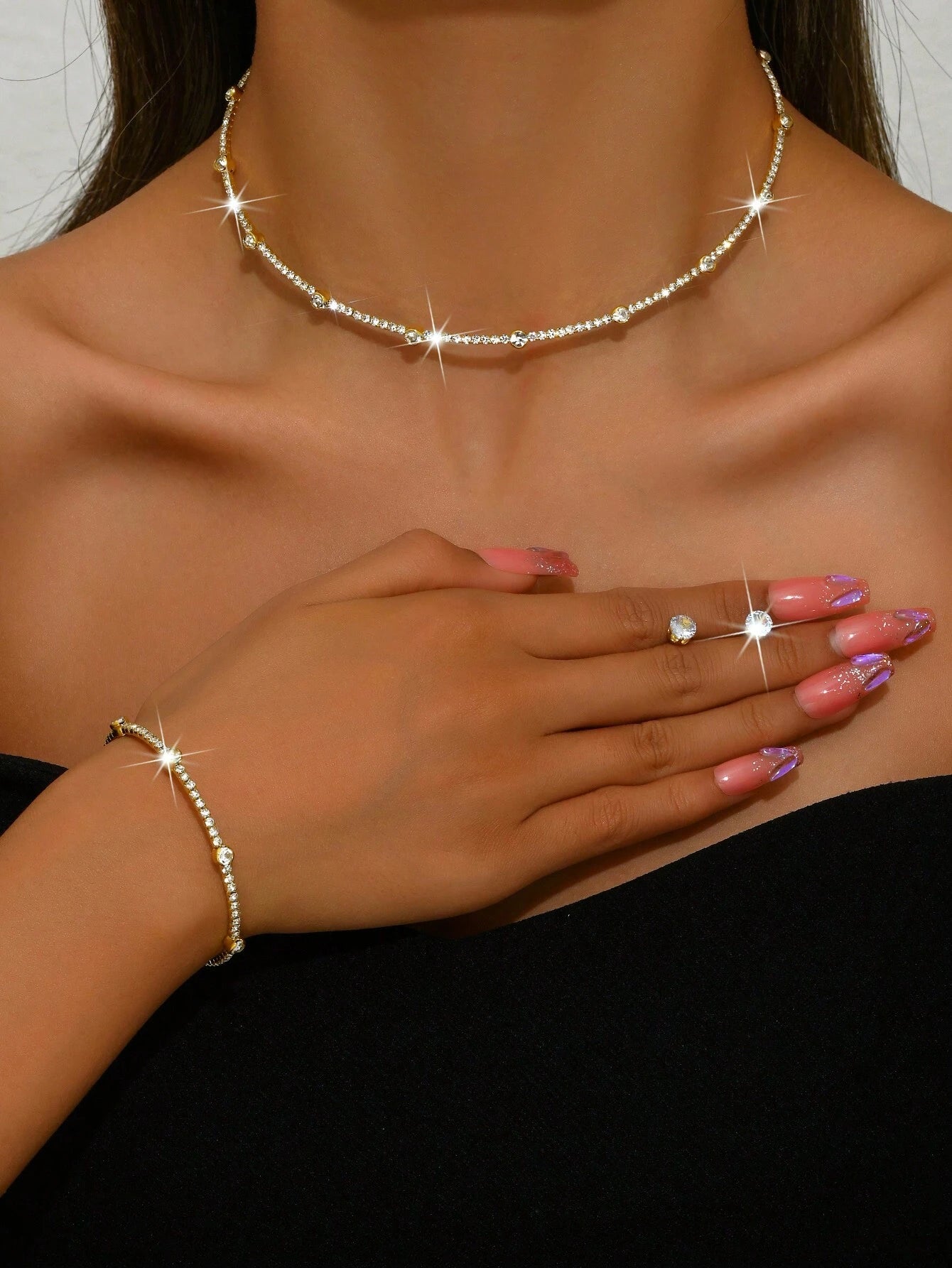Close-up of a woman's hand wearing a bracelet, ring, and necklace with sparkling stones.