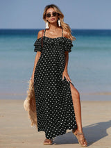Woman in a black polka dot dress standing on a beach with ocean in the background