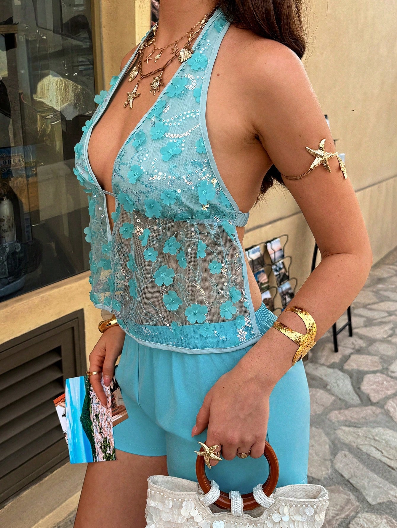 Person wearing a light blue lace top and shorts with gold accessories.
