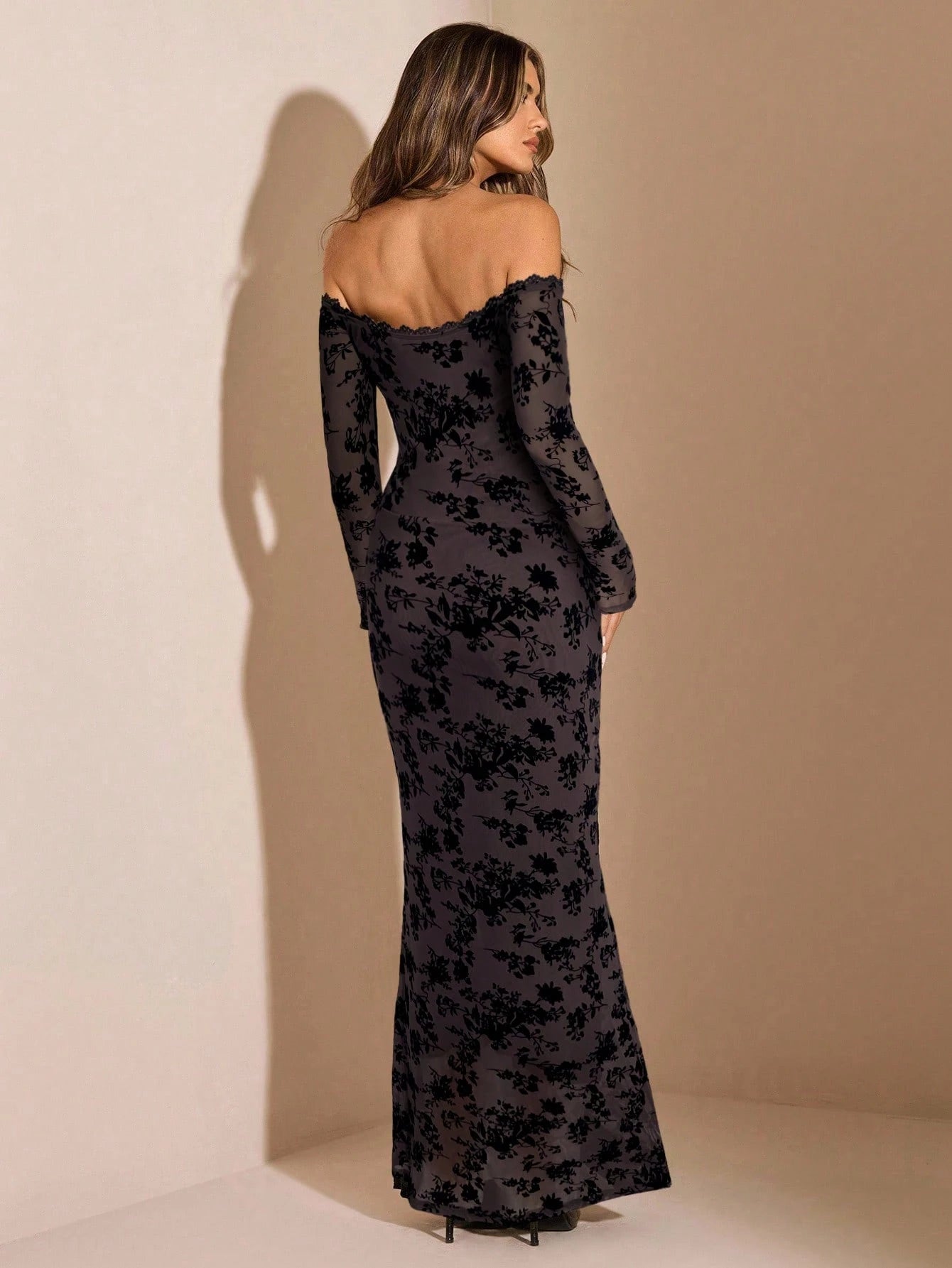 Woman wearing a black floral off-shoulder gown against a beige background
