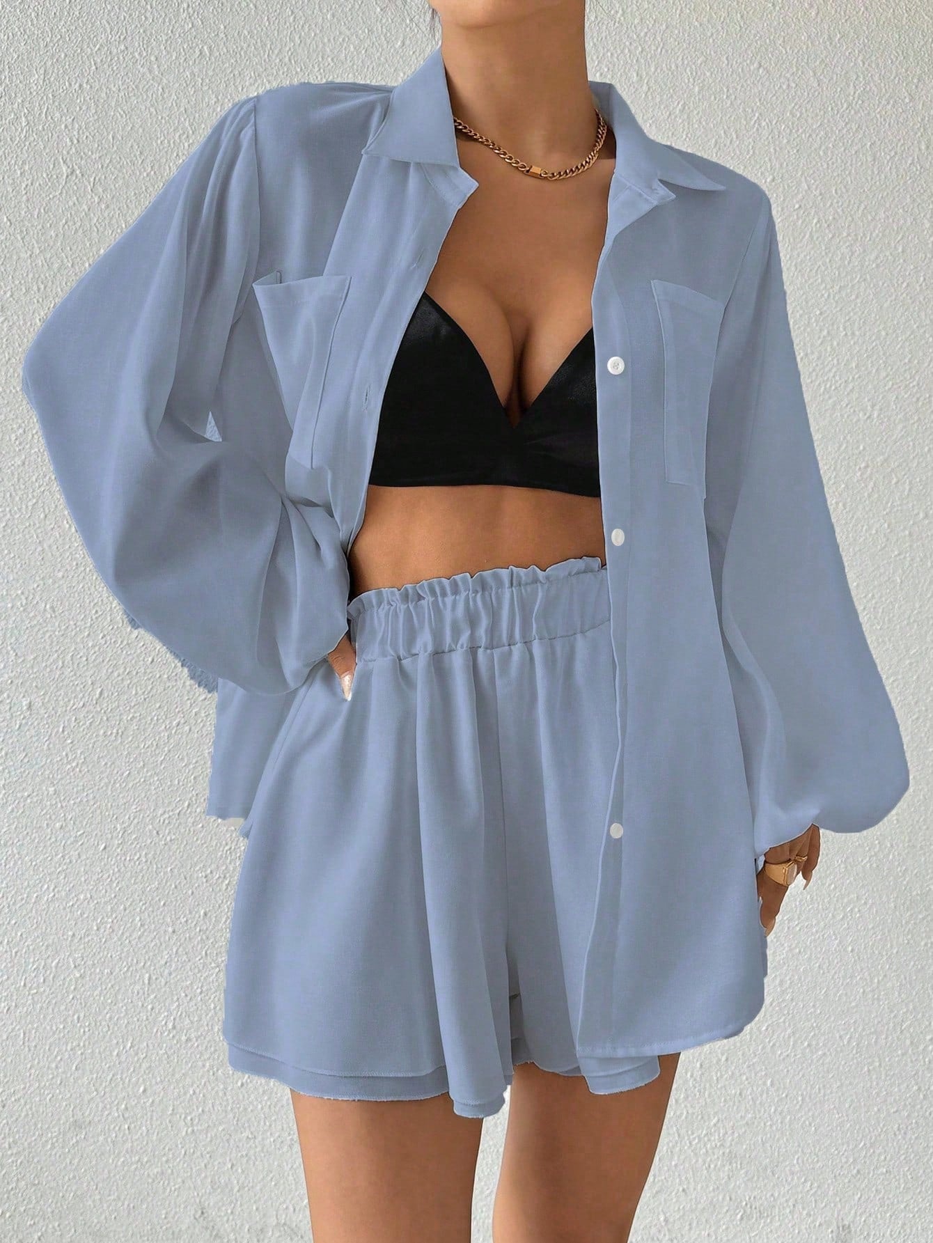 Person wearing a light blue shirt and shorts with a black bralette against a plain background