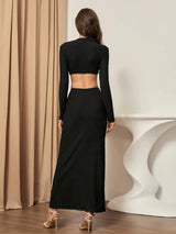 Woman wearing a black long-sleeve top and black skirt standing in front of a beige curtain.