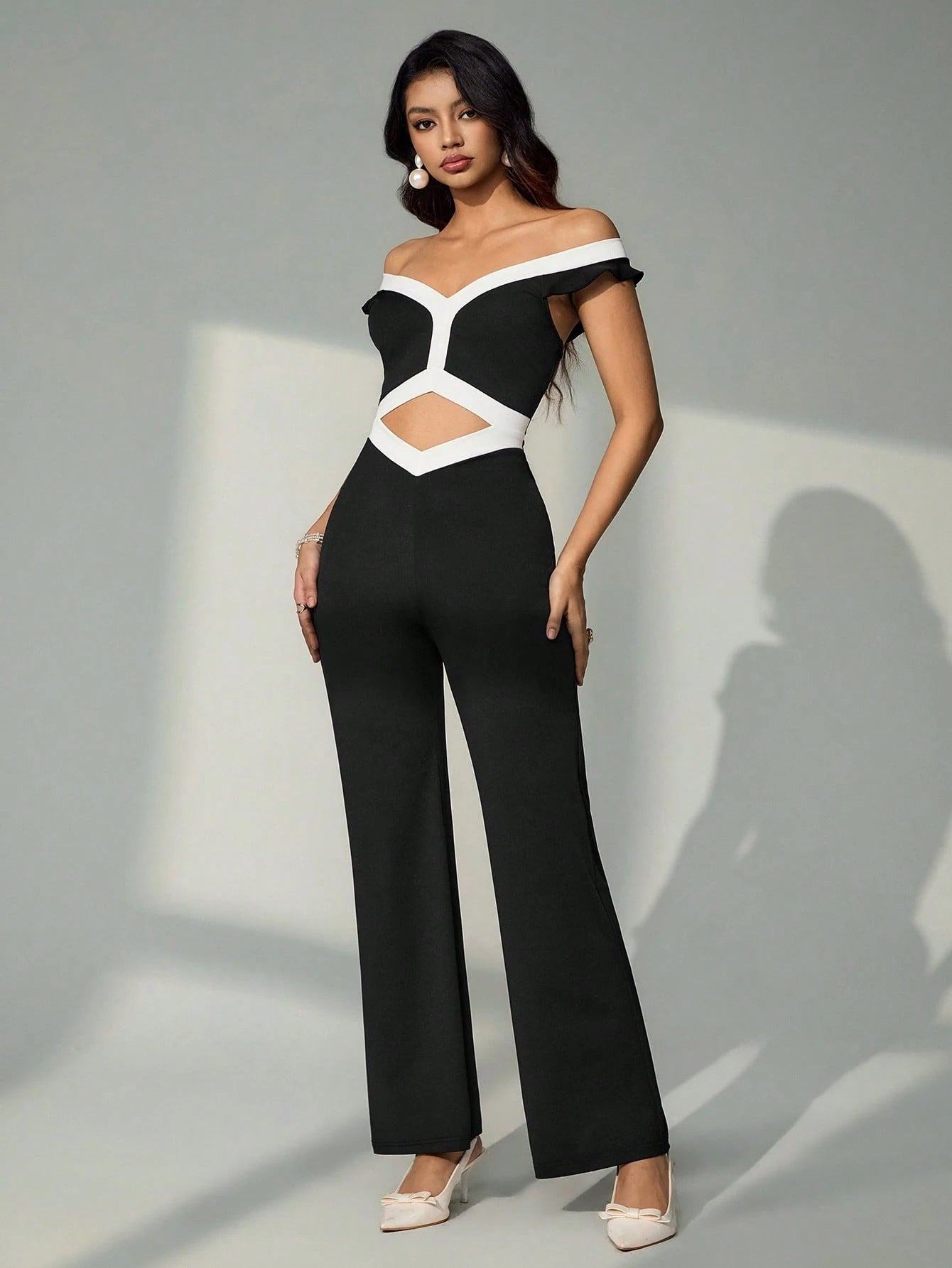 Woman wearing a black and white off-shoulder jumpsuit on a gray background