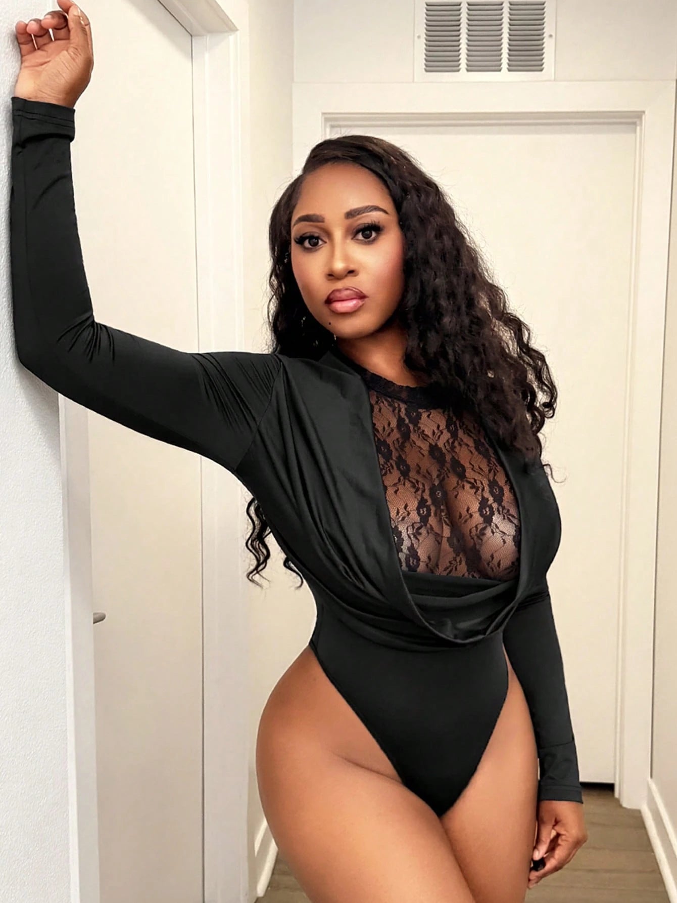 Woman wearing a black lace bodysuit in a room.