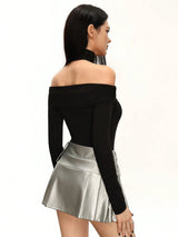 Woman wearing a black off-shoulder top and silver pleated skirt on a white background