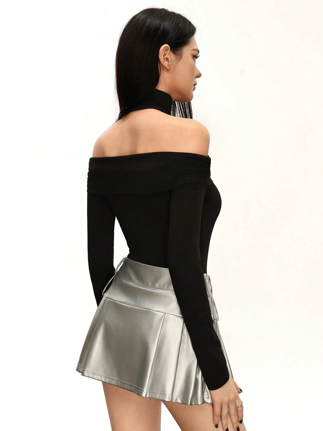 Woman wearing a black off-shoulder top and silver pleated skirt on a white background