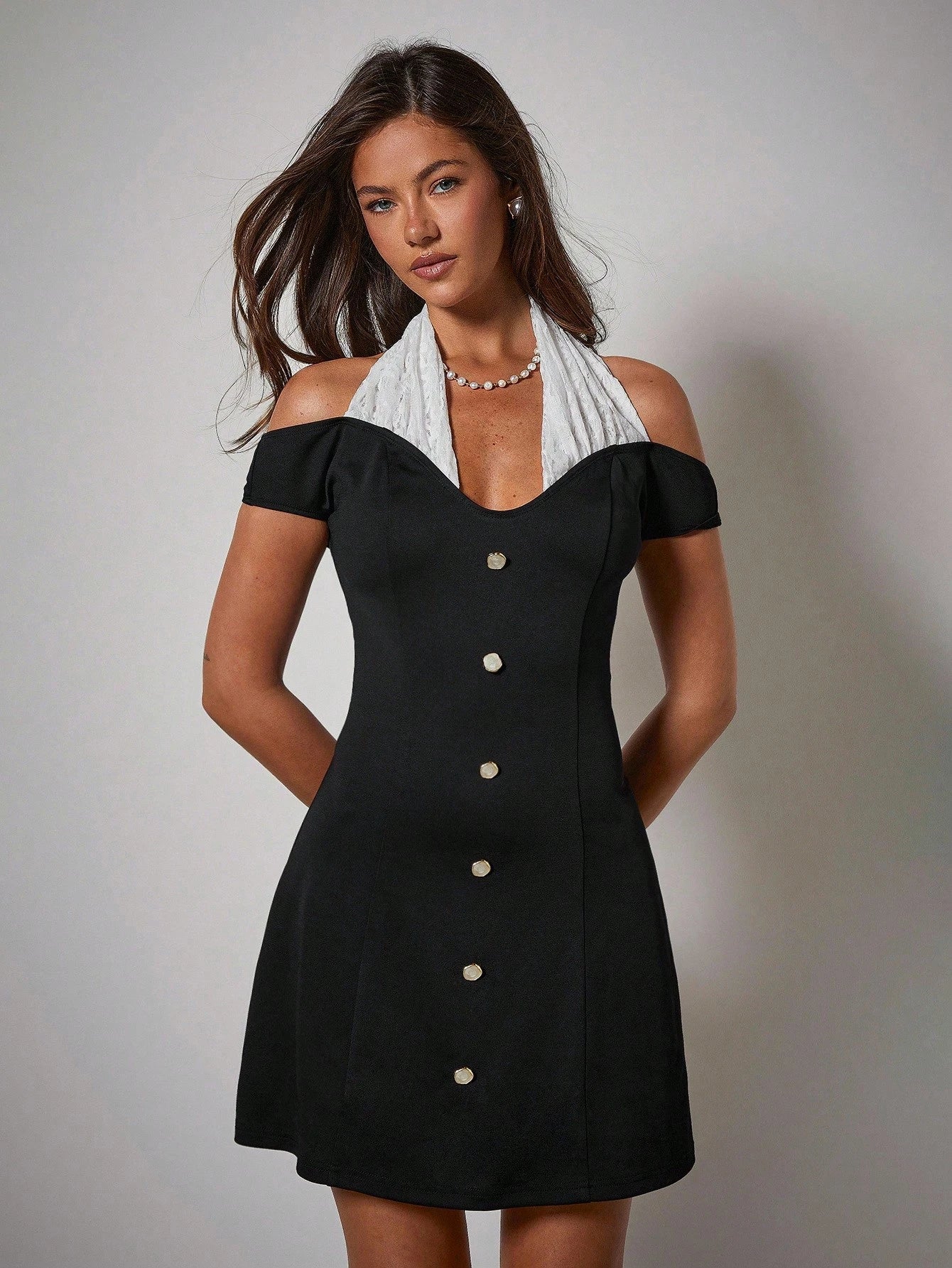 Woman wearing a black dress with white buttons and a white scarf on a gray background