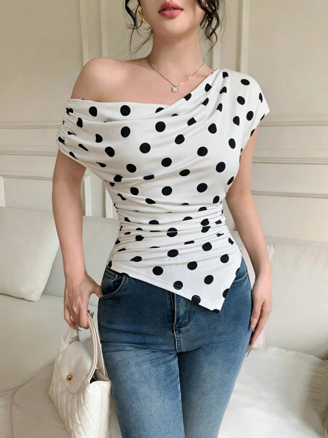 Woman wearing a white top with black polka dots and blue jeans indoors.