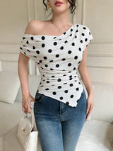 Woman wearing a white top with black polka dots and blue jeans indoors.