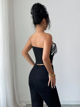 Woman wearing a black strapless top with zebra pattern and high-waisted black pants against a white wall.