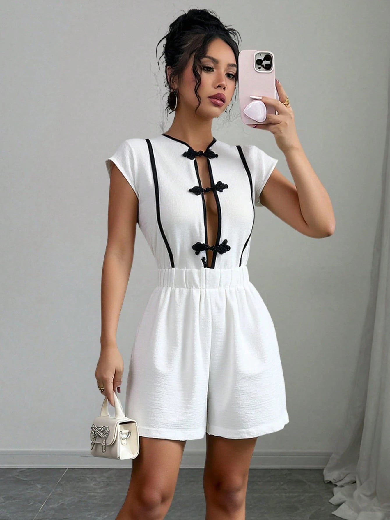 Woman taking a mirror selfie wearing a white romper with black accents.