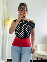 Person wearing a black polka dot top with a red waistband and light blue jeans, taking a mirror selfie.