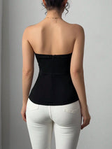 Person wearing a black strapless top and white pants against a gray background