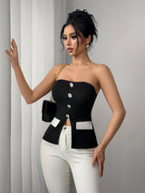 Woman wearing a black strapless top with white accents and white pants against a gray background