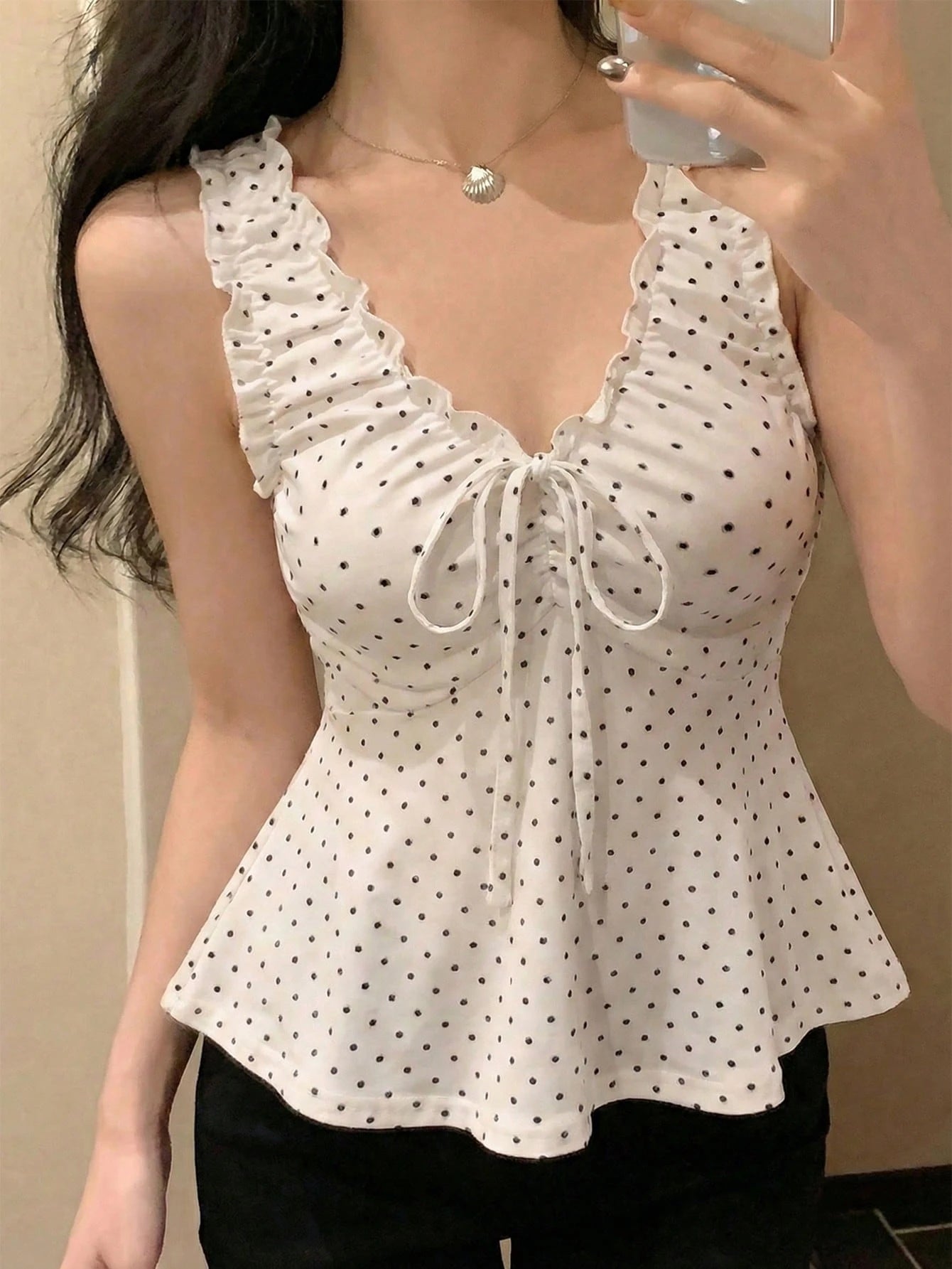 White polka dot top worn by a person against a neutral background