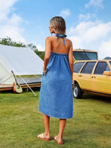 Woman in a blue dress standing in a grassy area with a tent and yellow car in the background.