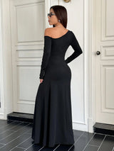 Woman wearing a black off-shoulder long-sleeve gown in a room with white walls and black tiles.