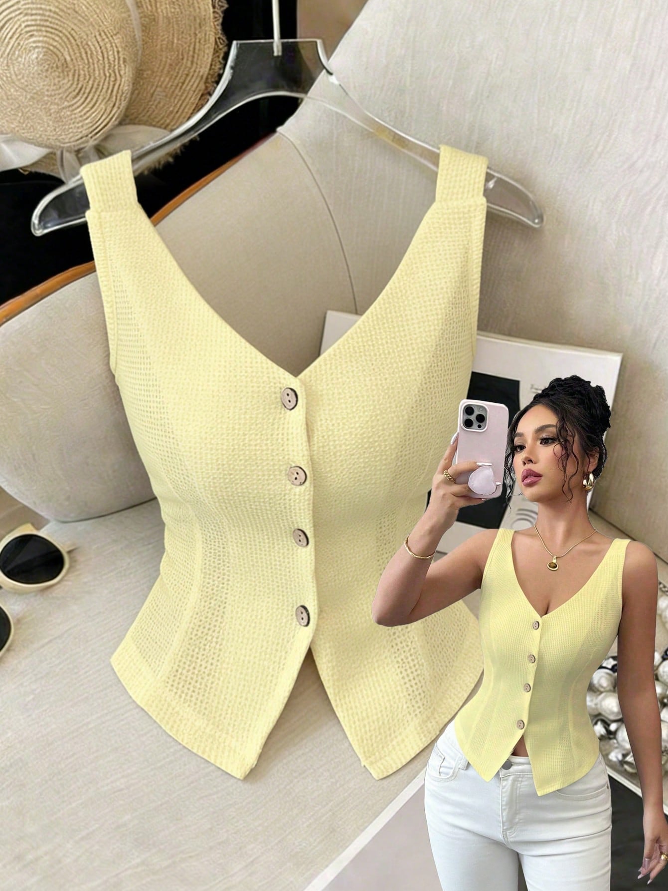 Woman taking a mirror selfie wearing a yellow button-up top, with a matching vest on a hanger in the background.