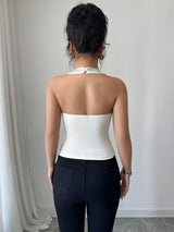 Person wearing a white halter top and black pants against a plain background