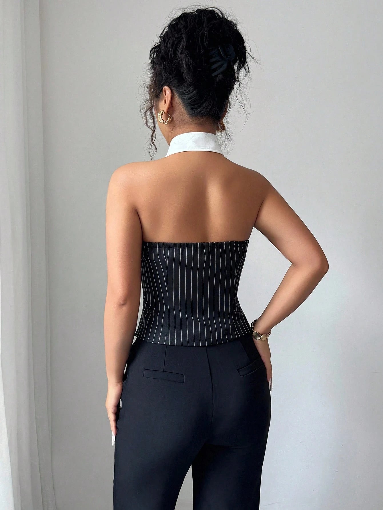 Woman wearing a black pinstripe corset and high-waisted pants against a plain background