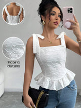 Woman wearing a white top with ruffled details, taking a selfie in a room.