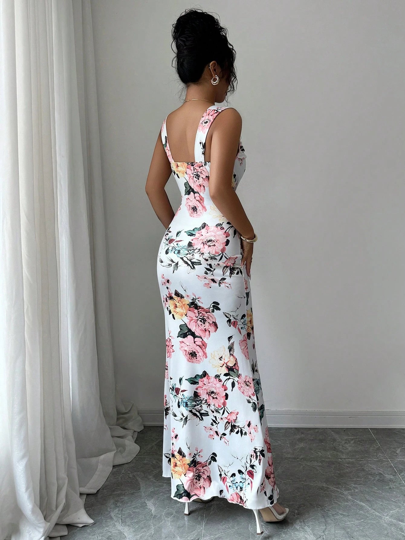 Woman wearing a floral dress standing in a room with white curtains.