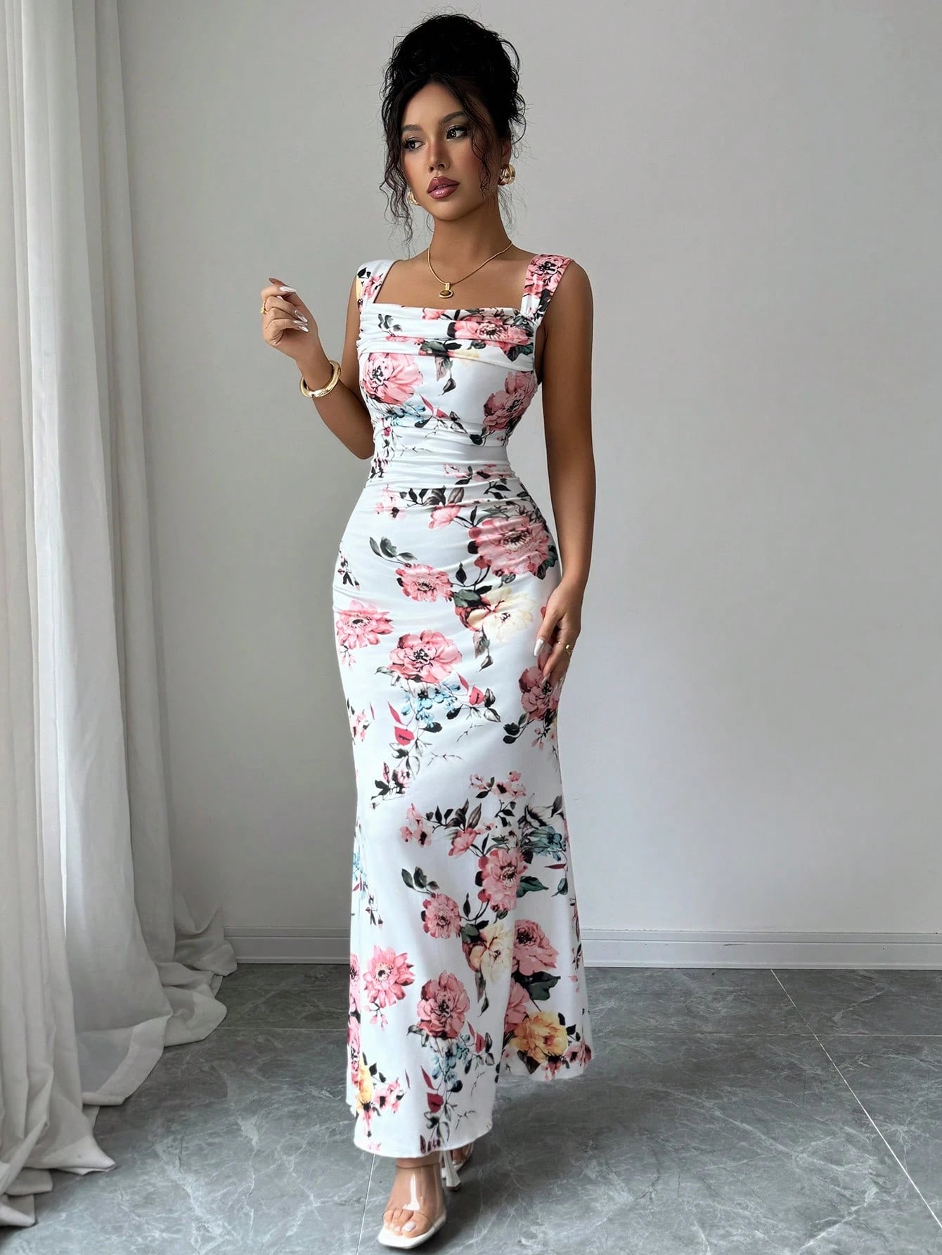 Woman wearing a floral dress standing in a room with white curtains and gray floor.