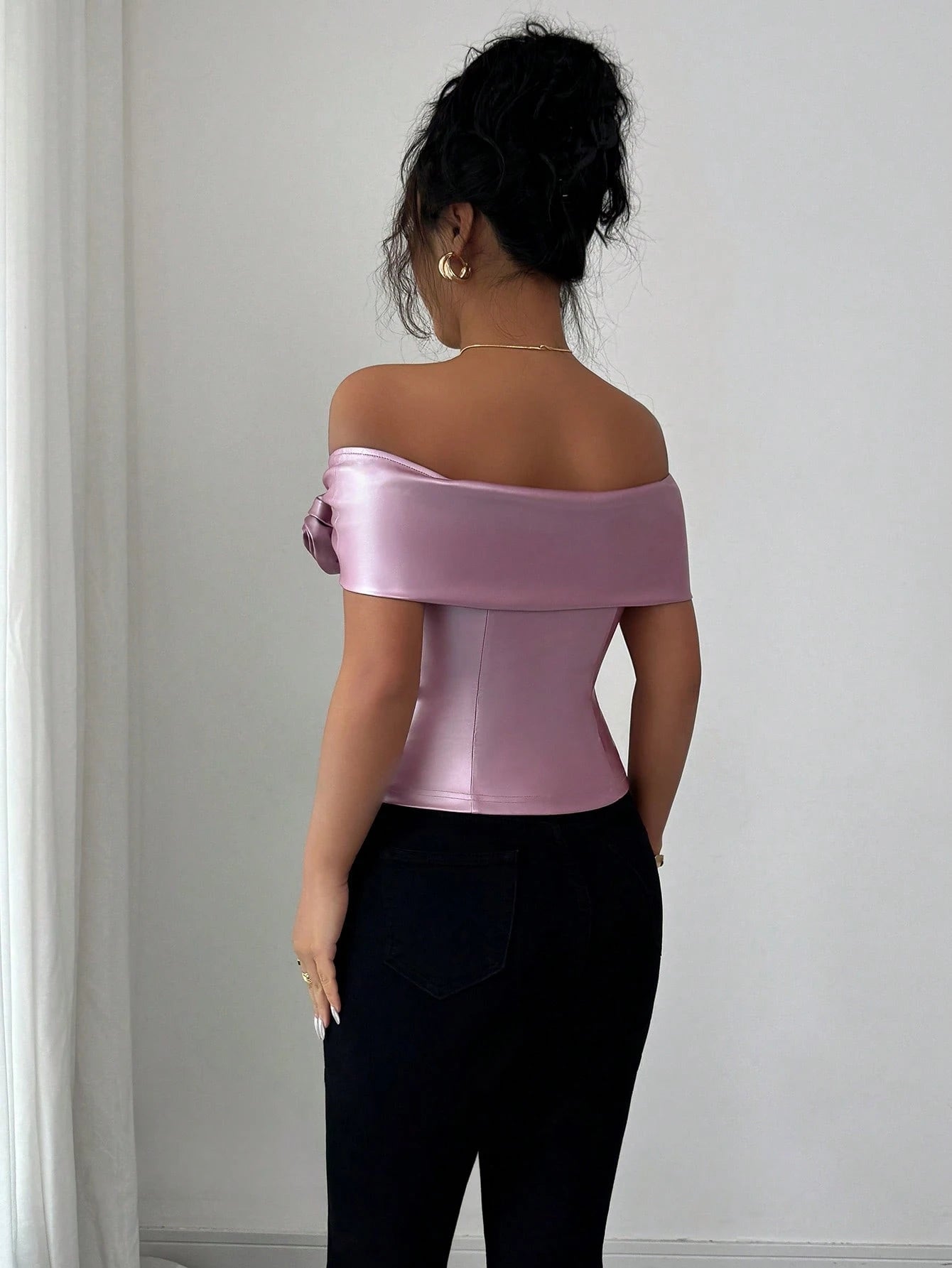 Woman wearing a pink satin off-shoulder top against a white wall