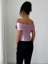 Woman wearing a pink satin off-shoulder top against a white wall