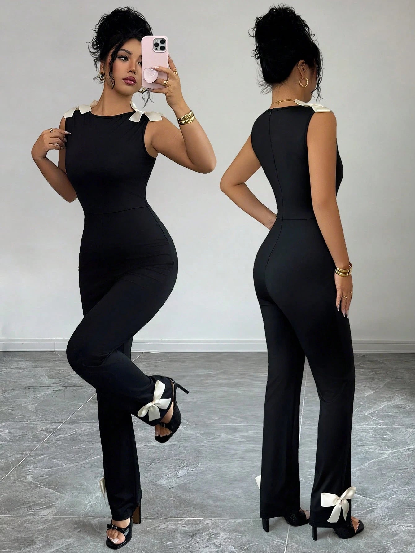 Woman wearing a black jumpsuit taking a mirror selfie.