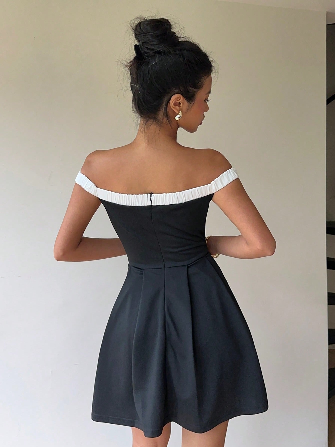 Woman wearing a black off-shoulder dress with white trim against a plain background