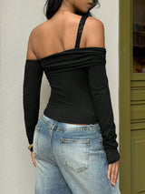 Person wearing a black off-shoulder top and blue jeans against a neutral wall.