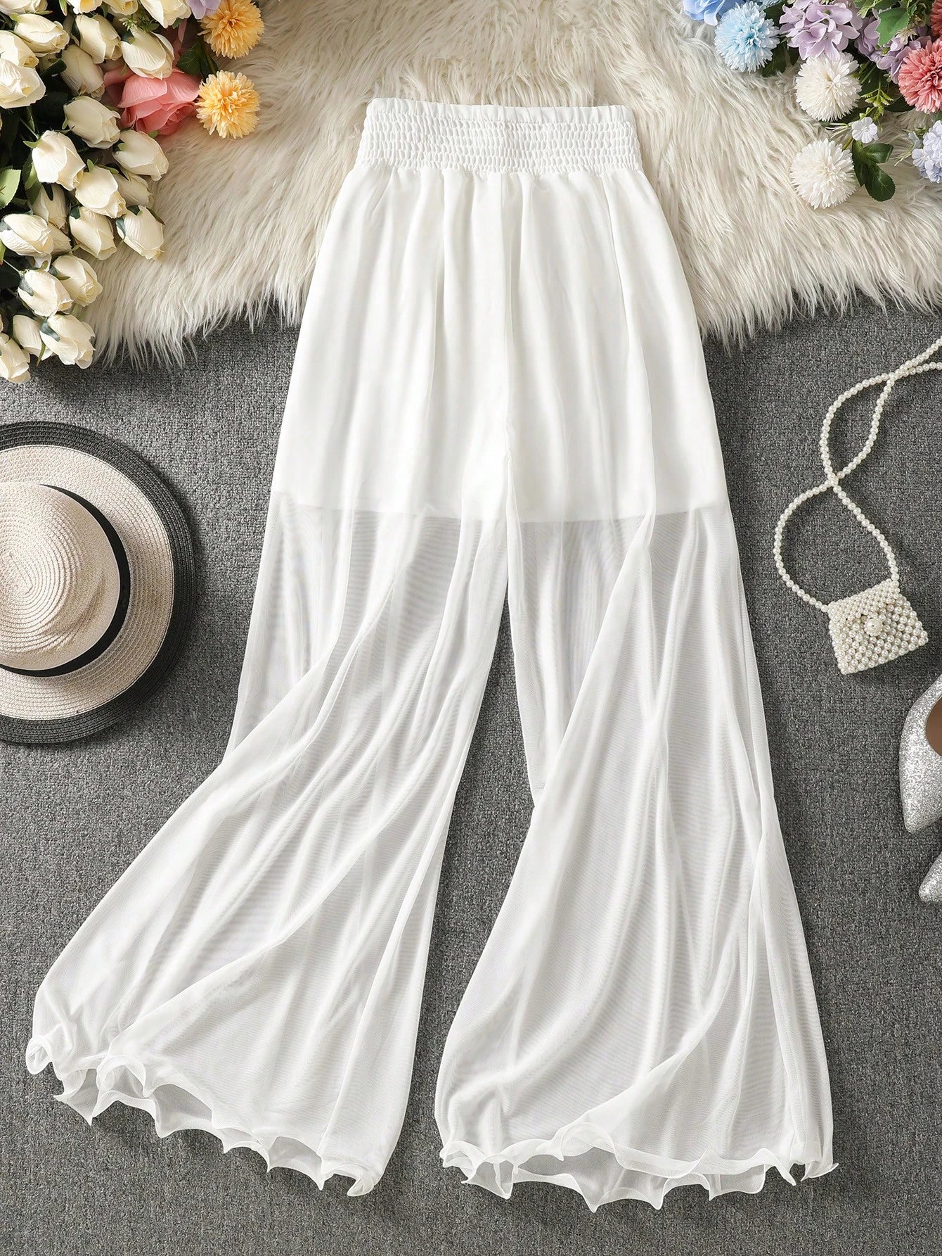 White wide-leg pants on a gray surface with decorative items like flowers and a hat.