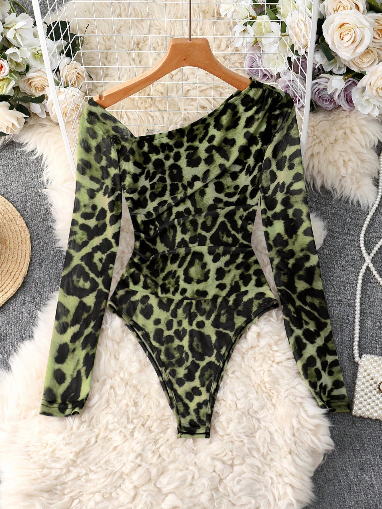 Green leopard print bodysuit on a hanger with decorative background