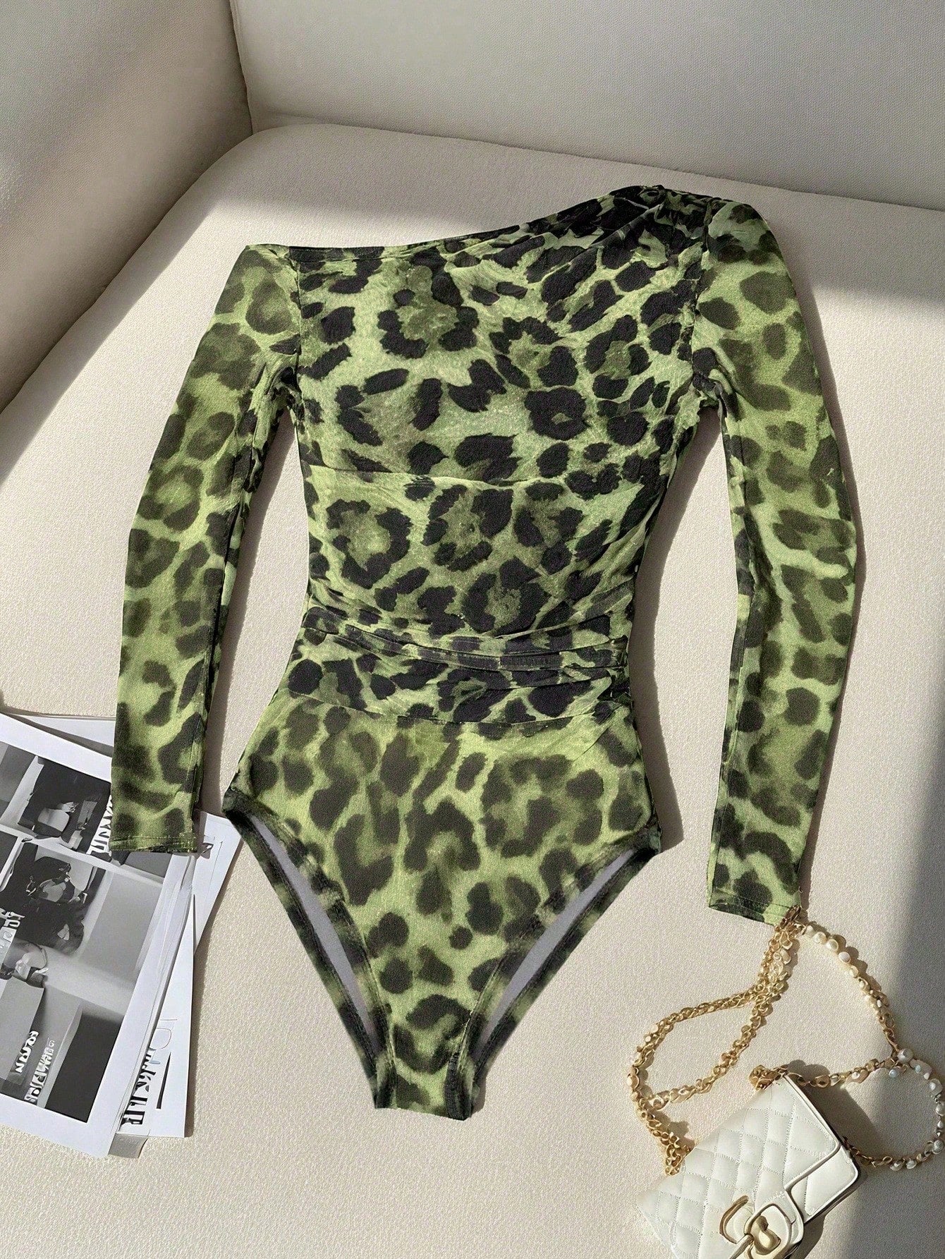 Green leopard print bodysuit on a light-colored surface with a handbag and magazine.
