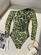 Green leopard print bodysuit on a light-colored surface with a handbag and magazine.