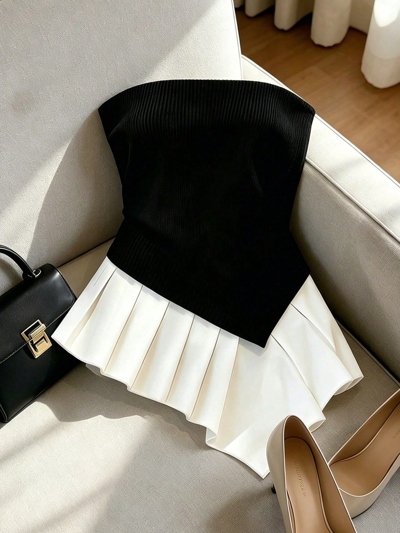Black top and white skirt on a chair with a black handbag and beige shoes nearby.