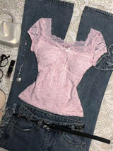 Pink lace top and blue jeans on a textured surface with a handbag and other items.