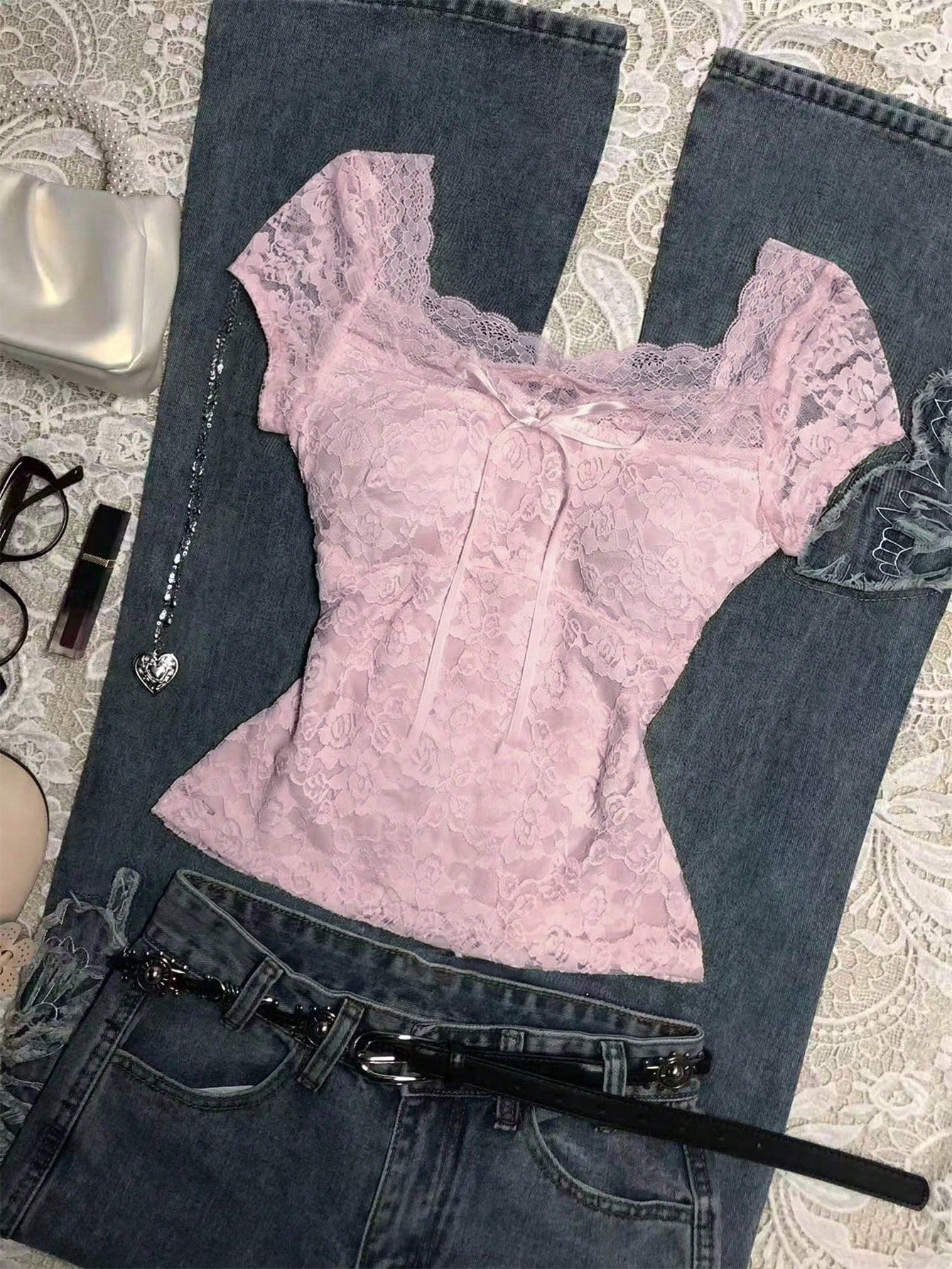 Pink lace top and blue jeans on a textured surface with a handbag and other items.