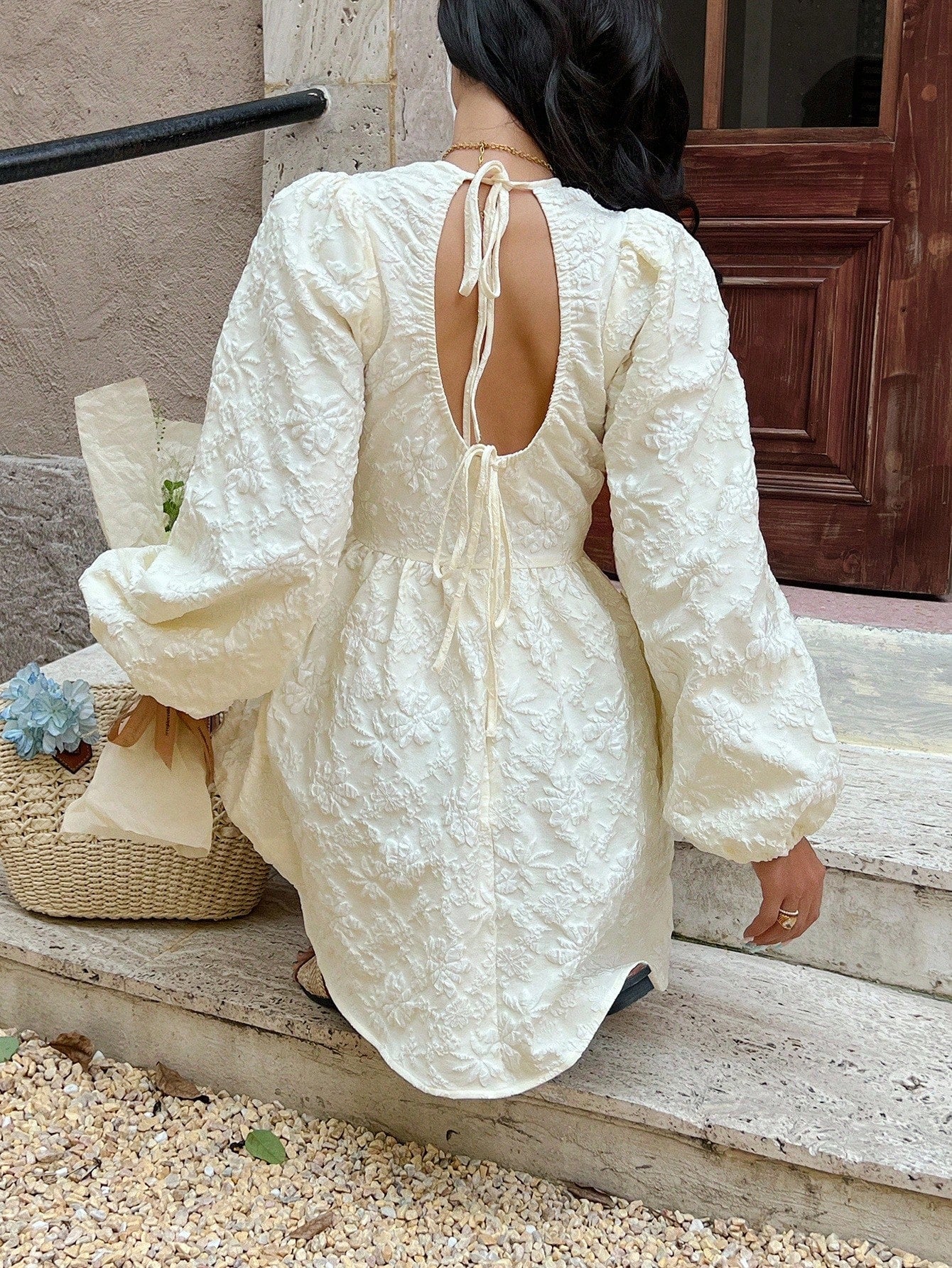 Person wearing a white lace dress sitting on steps outdoors.